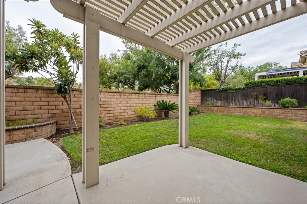 Spacious backyard with mature landscaping, block-wall fencing, and a covered patio retreat.