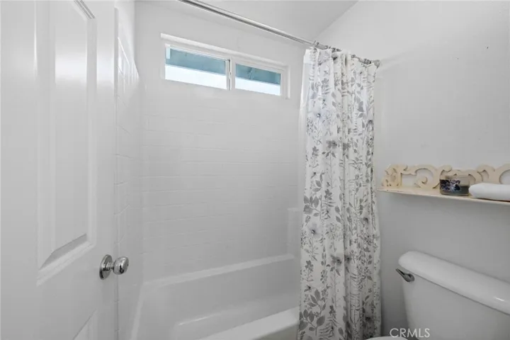 Hall bathroom featuring shower-in-tub combo with a bright window and vinyl plank flooring.