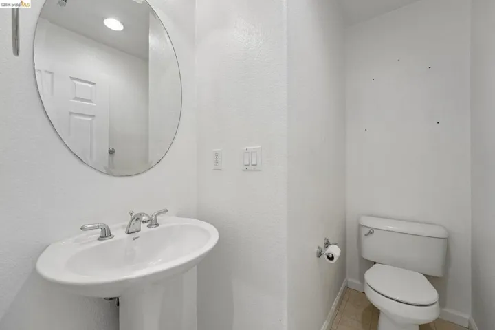 Pedestal sink with chrome faucet, oval mirror, recessed lighting, and light-toned tile flooring