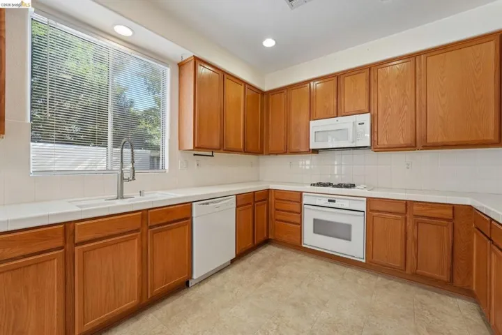 Kitchen featuring wood cabinetry, white tile countertops, a white tile backsplash, and white appliances