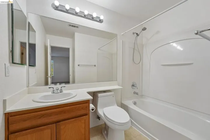 Bathroom featuring a wood-finish vanity with an integrated sink, a large wall-mounted mirror, and overhead strip lighting