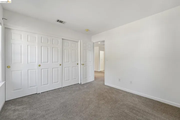 Bedroom featuring light grey carpeting, white walls, and a multi-panel sliding closet door system with brass hardware