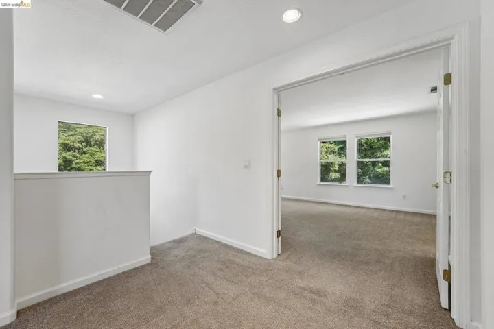 Carpeted interior area with white walls and trim, featuring a partial wall partition, recessed lighting, and a window overlooking lush greenery