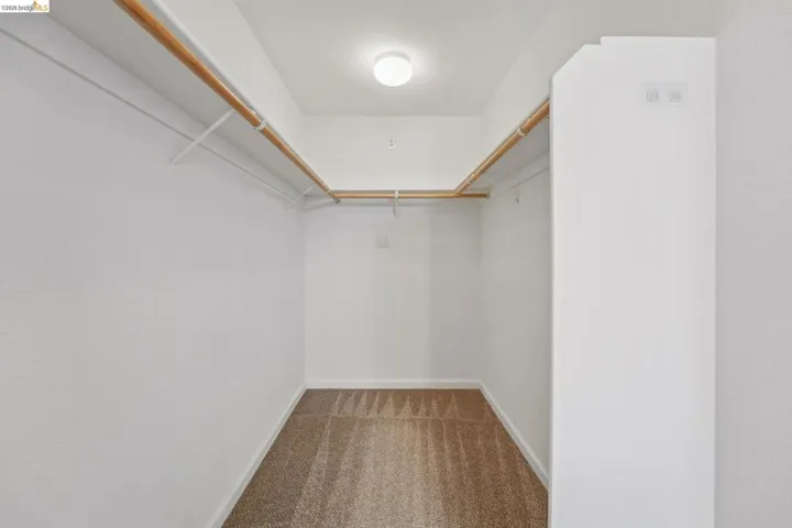 Walk-in closet featuring built-in wood hanging rods, white wire shelving, recessed ceiling light, and neutral-toned carpeting