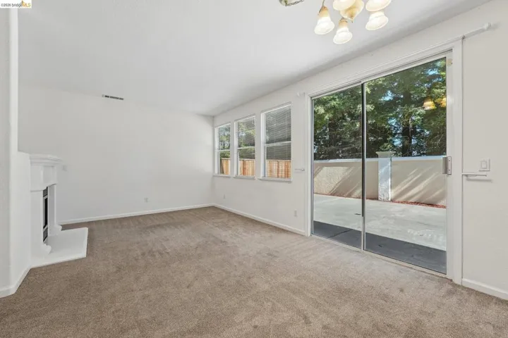 Carpeted living area featuring a white mantel fireplace, a series of transom windows, and a glass sliding door opening to an outdoor patio with a privacy wall