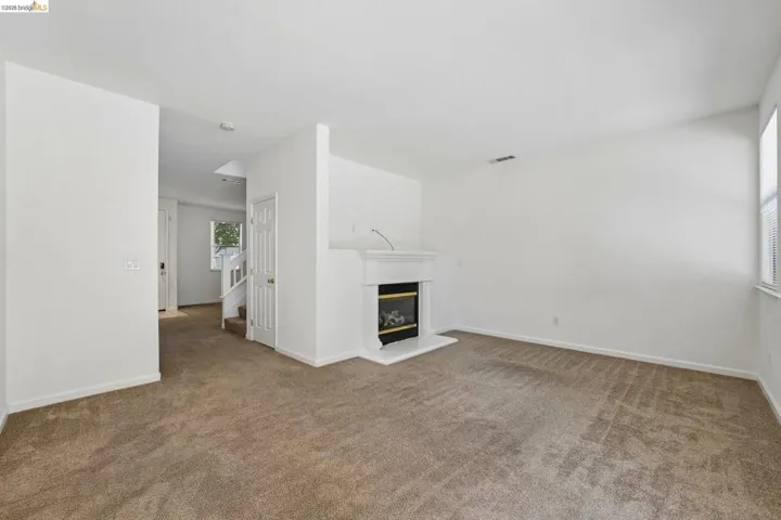 Carpeted living area featuring a white mantel fireplace, a window with horizontal blinds, and neutral painted walls