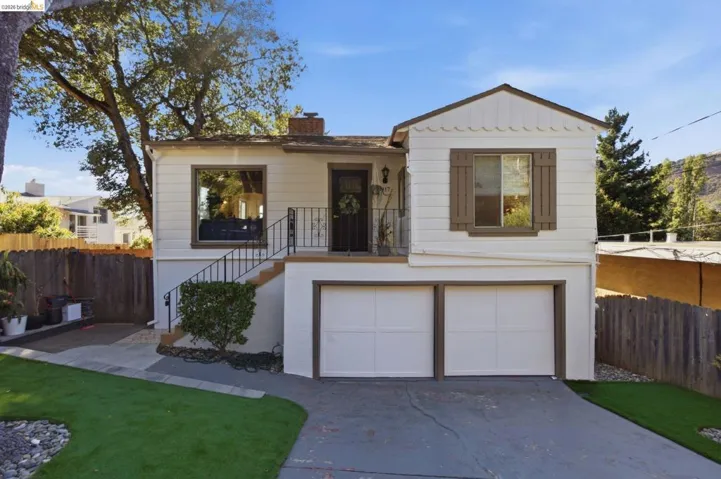 Two-story residence featuring white siding, a prominent front entrance with a metal railing staircase, and a dual-door integrated garage