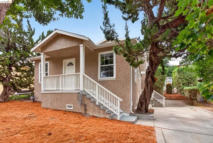 Stucco-clad exterior featuring a covered front porch with white railings, a concrete driveway, and mature landscaping