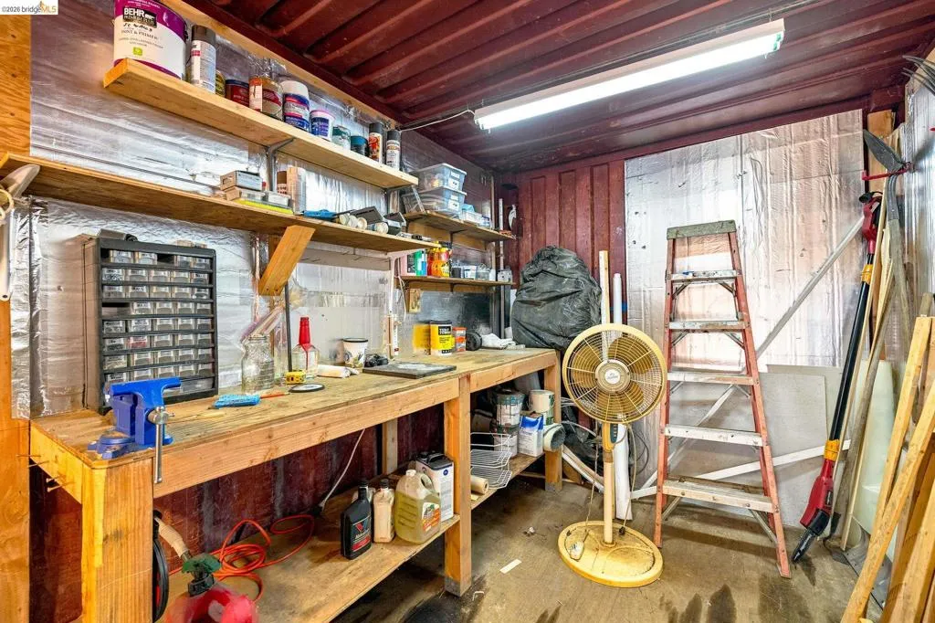 Utility space featuring a wood workbench with integrated shelving, overhead fluorescent lighting, and corrugated metal walls