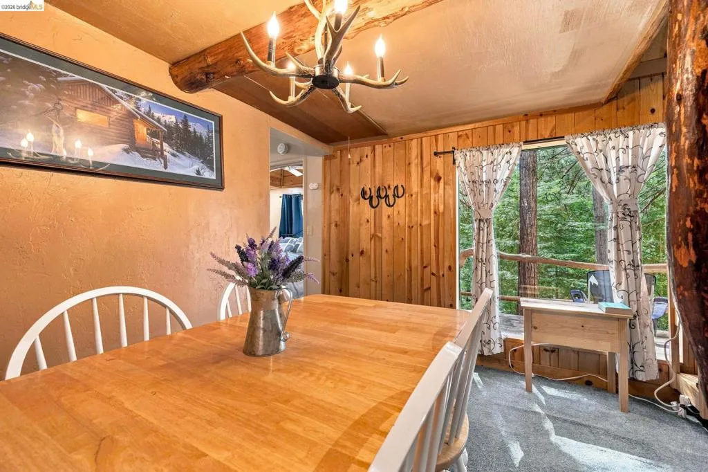 Dining area featuring a wood-finish dining table, a rustic antler-style chandelier, and a wood-paneled wall
