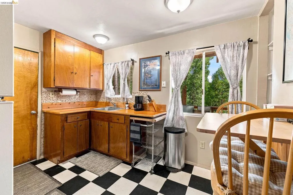 Kitchen featuring black and white checkerboard flooring, natural wood cabinetry, wood countertops, and a window with outdoor tree scenery