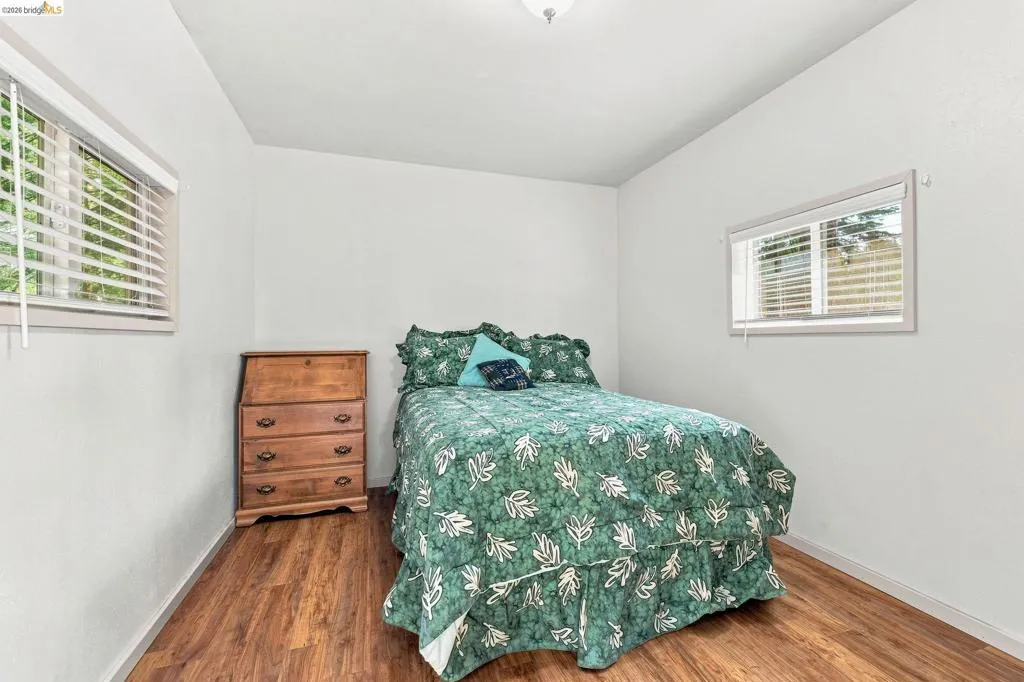 Room with wood-finish flooring, white walls, and two windows with blinds