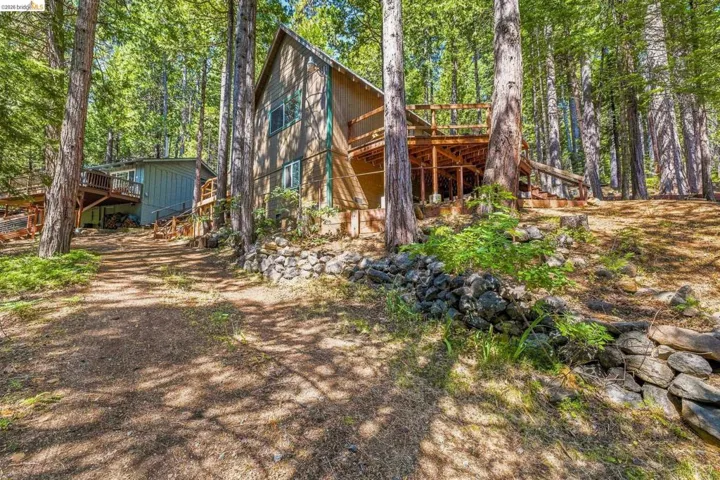 Wooded property featuring a two-story home with a gabled roofline and an expansive elevated deck