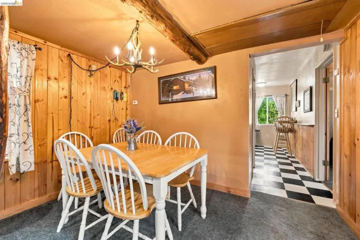 Dining area featuring wood paneling, a distinctive antler-style chandelier, and a wood beam accent