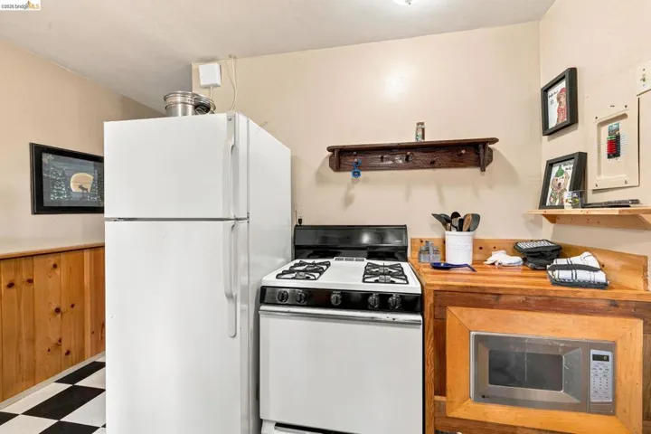 Compact kitchen featuring a checkerboard floor, wood paneling, white refrigerator, white gas range, and built-in microwave