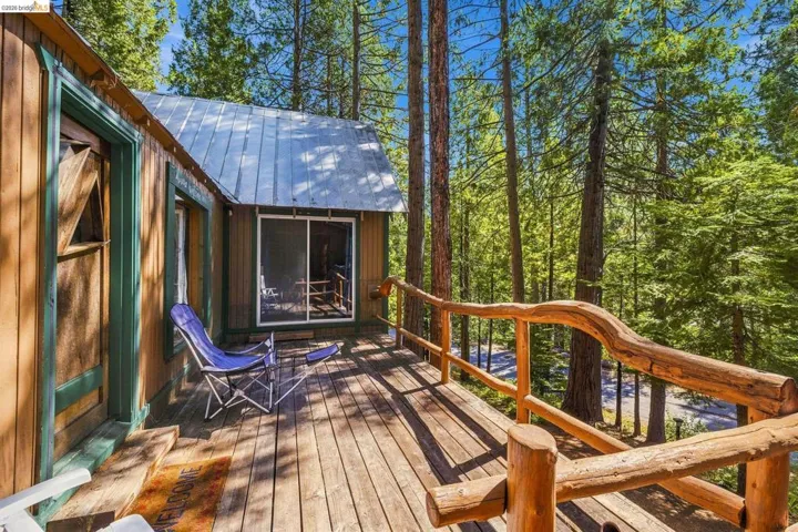 Elevated wood deck featuring a natural log railing system, wood siding, and abundant surrounding mature trees
