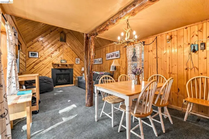 Open concept living and dining area featuring wood paneling throughout, a vaulted ceiling, and grey carpeting