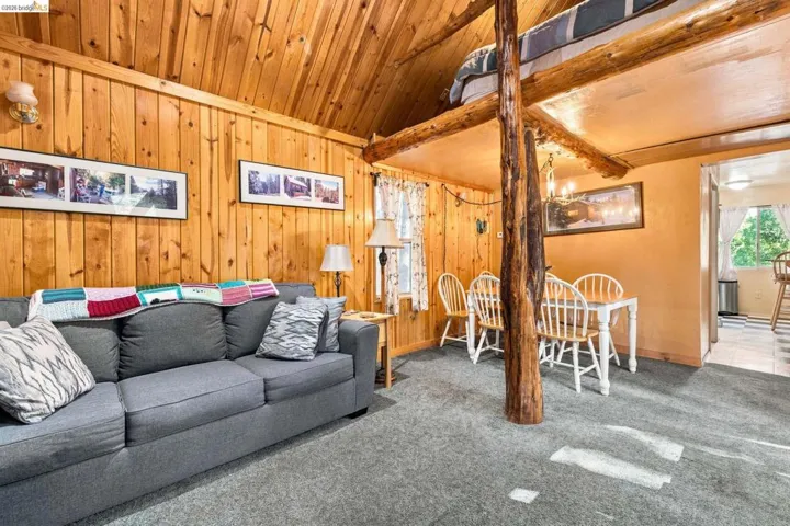 Vaulted wood-paneled ceiling, wood-plank wall finishes, gray carpet flooring, wood support beams, and an open loft area