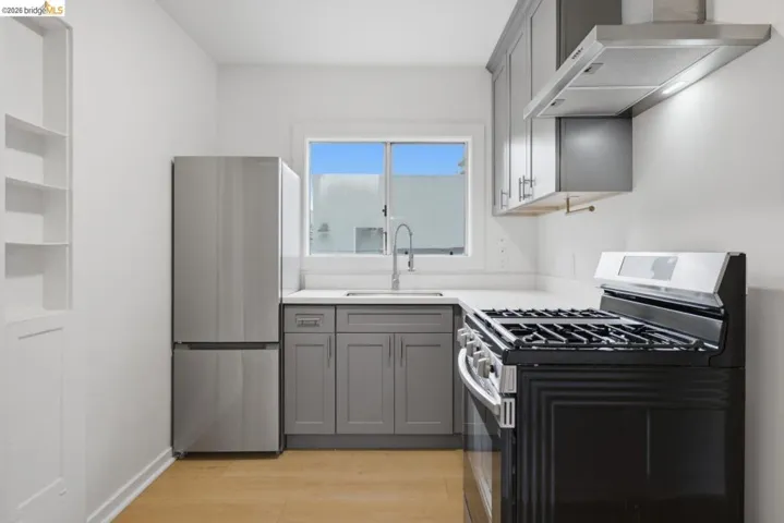 Kitchen featuring a stainless steel refrigerator, gas range, gray cabinetry, light-toned countertops, and wood-finish flooring