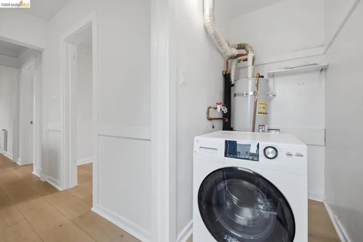 Dedicated laundry area with a front-loading washing machine, overhead water heater, and wood-finish flooring