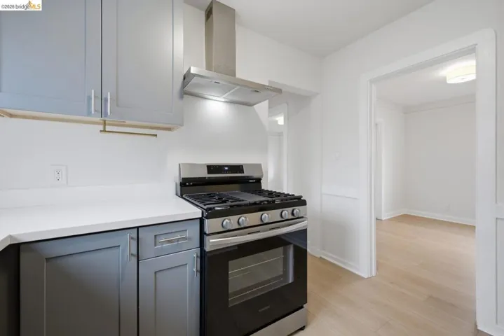 Modern kitchen featuring stainless steel range with overhead ventilation, light grey cabinetry, white countertops, and light wood-finish flooring