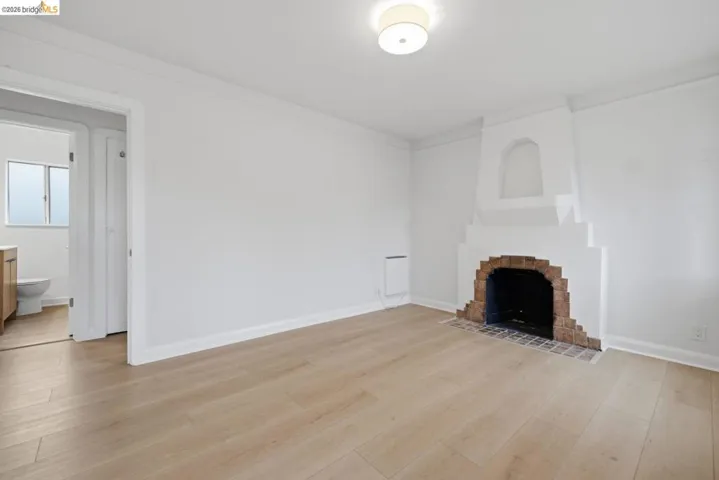 Spacious room featuring light wood-finish flooring, a decorative fireplace with a brick hearth, and a contemporary flush-mount ceiling light fixture