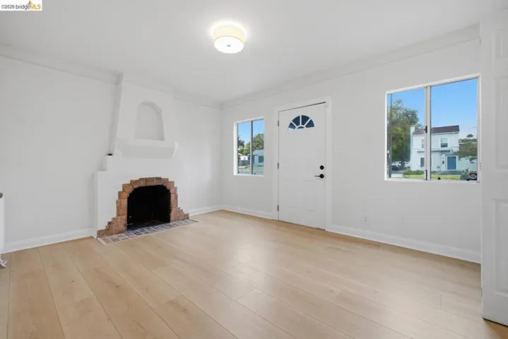 Living space featuring a brick-lined fireplace, wood-finish flooring, white walls, and multiple windows