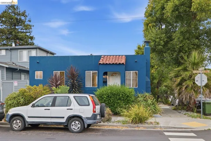 Blue stucco exterior featuring a red tile entryway awning, multiple windows, and a side chimney