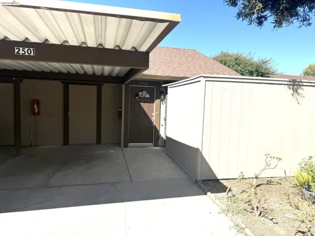 Covered carport area featuring a brown entry door with decorative glass, an exterior light fixture, and an attached storage shed