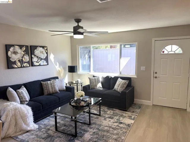 Living area featuring light wood-finish flooring, a window offering natural light, and a ceiling fan with integrated lighting