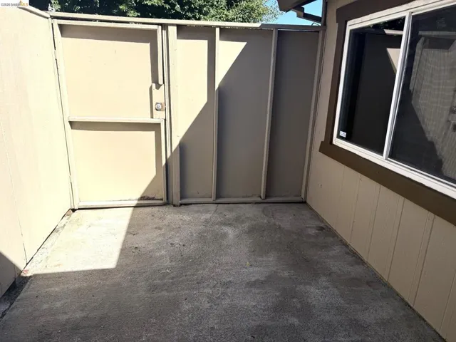 Enclosed outdoor patio featuring a concrete surface, a side gate, and a window with white trim