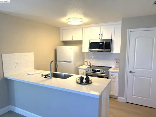 Kitchen featuring a stainless steel sink with a gooseneck faucet, white shaker cabinetry, stainless steel microwave, and a subway tile backsplash