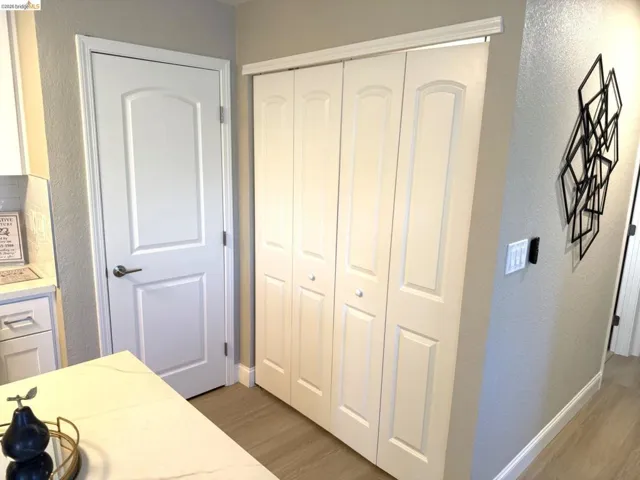 White bifold doors with arched paneling, light wood-finish flooring, and a solid white interior door with brushed nickel hardware