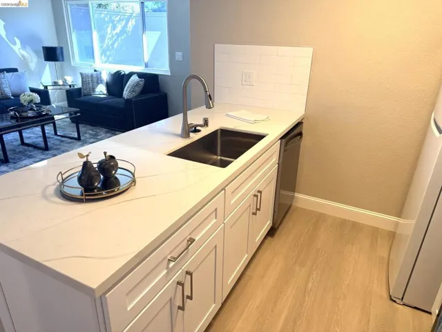 Kitchen island featuring a stainless steel sink with a high-arc faucet, white shaker-style cabinetry, and a quartz countertop