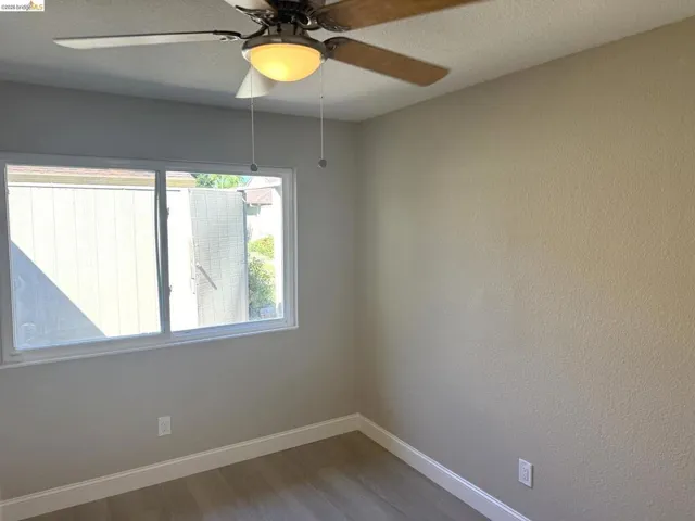 Contemporary room featuring a ceiling fan with integrated lighting, wood-finish flooring, and white baseboards