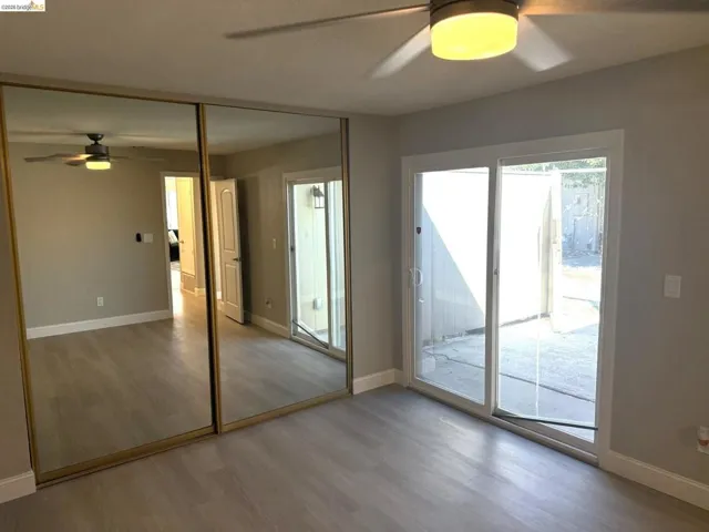 Spacious interior featuring light wood-finish flooring, sliding glass doors to outdoor space, mirrored closet doors, and a ceiling fan with integrated lighting