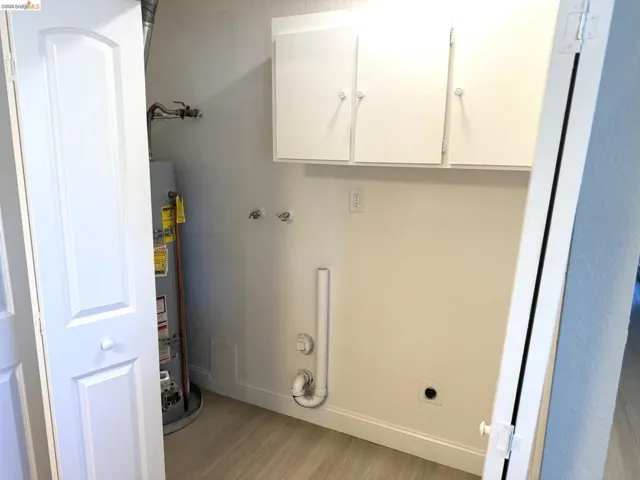 Utility space with wood-finish flooring, white baseboards, and overhead white cabinetry