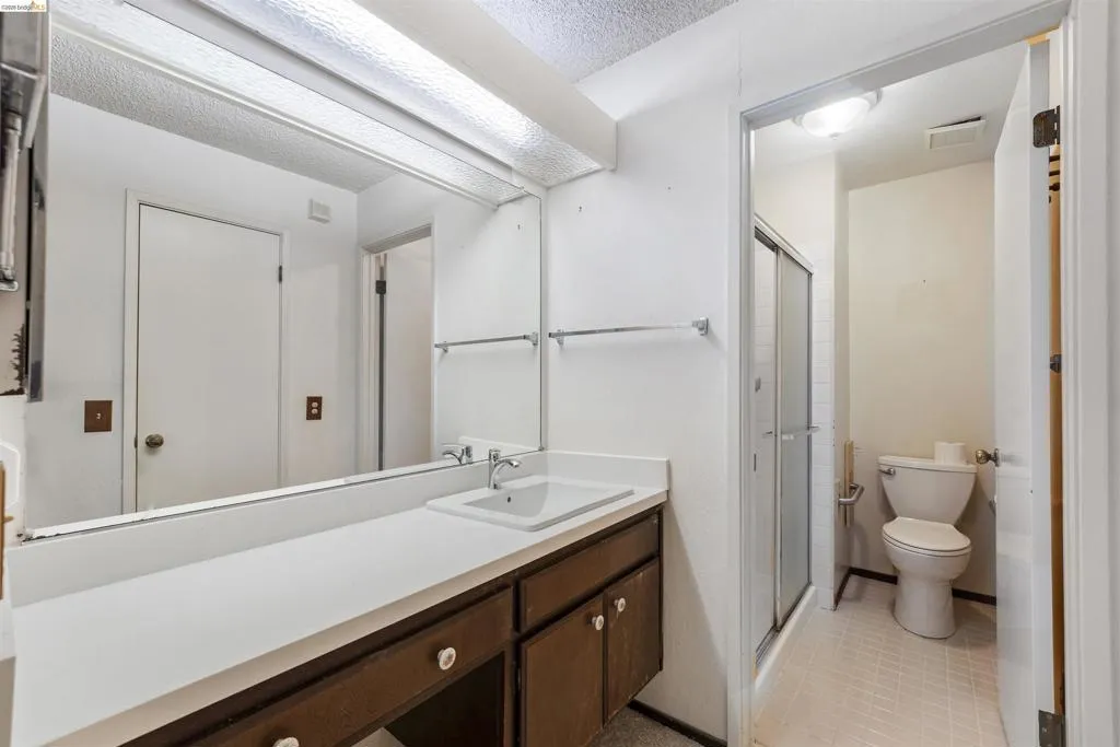 Bathroom featuring a vanity with a white countertop and dark wood-finish cabinetry, an integrated sink with a chrome faucet, and a large wall-mounted mirror Bathroom featuring a vanity with a white countertop and dark wood-finish cabinetry, an integrated sink with a chrome faucet, and a large wall-mounted mirror