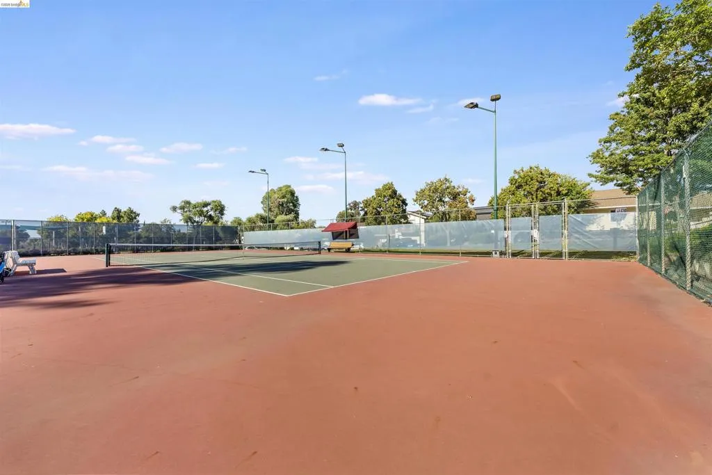 Tennis court featuring a green playing surface with white lines, surrounded by a red hard court Tennis court featuring a green playing surface with white lines, surrounded by a red hard court