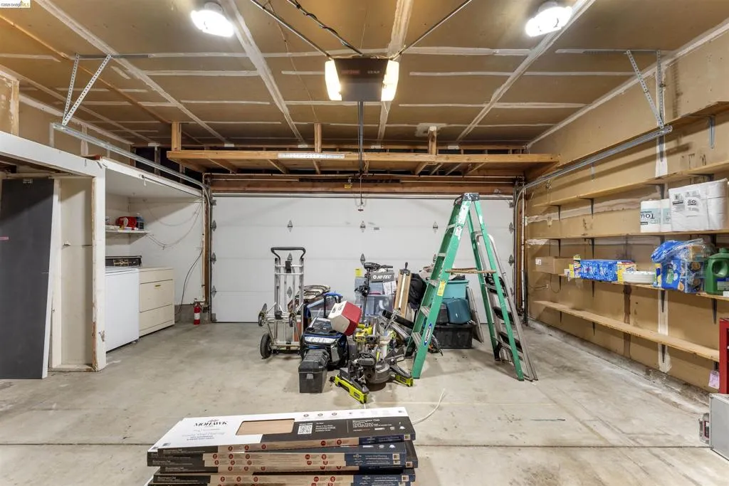 Spacious garage featuring a concrete floor, built-in shelving, overhead storage, and multiple lighting fixtures Spacious garage featuring a concrete floor, built-in shelving, overhead storage, and multiple lighting fixtures