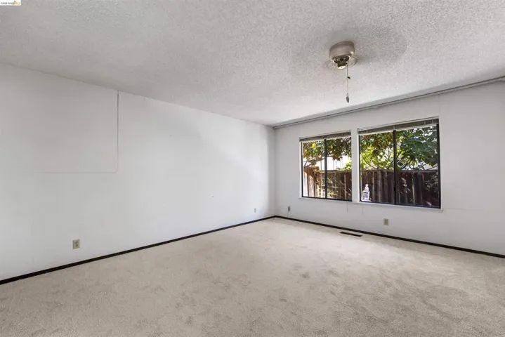 Spacious room featuring light-colored carpeting, white walls, and a textured ceiling
