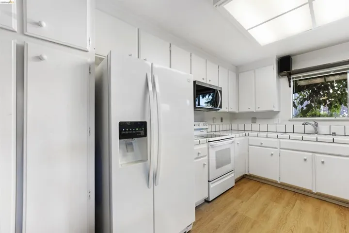 Kitchen featuring abundant white cabinetry, white appliances, wood-finish flooring, a white tile backsplash, and a window above the sink
