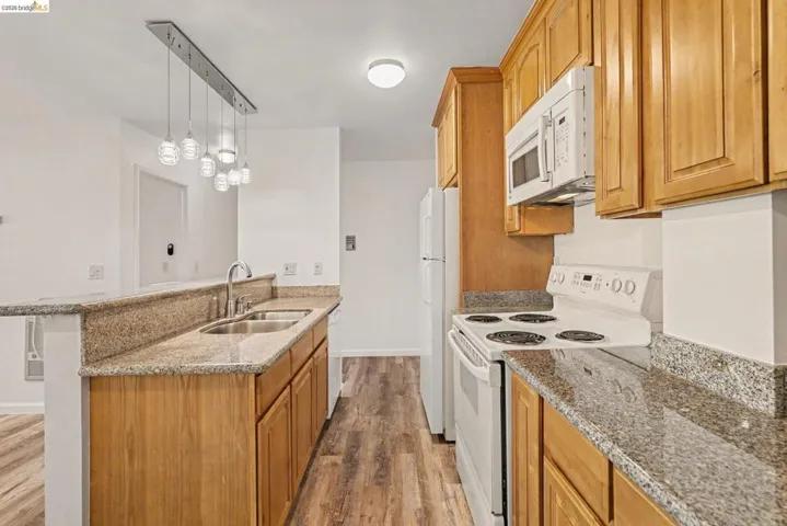 Kitchen featuring wood-finish flooring, granite countertops, double basin stainless steel sink with a high-arc faucet, and a range with an overhead microwave