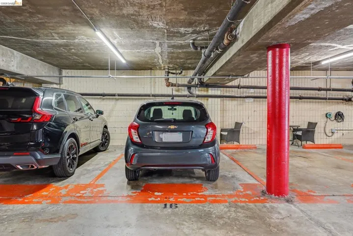 Dedicated parking space with concrete flooring, exposed overhead piping, and fluorescent lighting