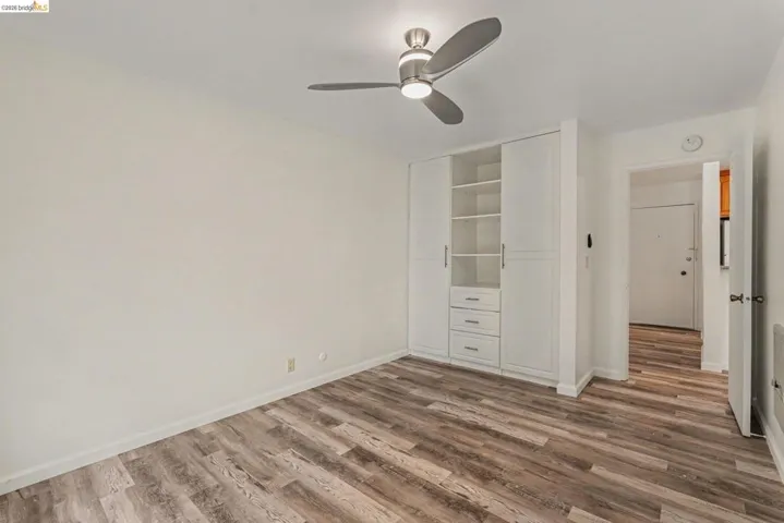 Interior space featuring wood-finish flooring, white walls, and a contemporary ceiling fan with integrated lighting