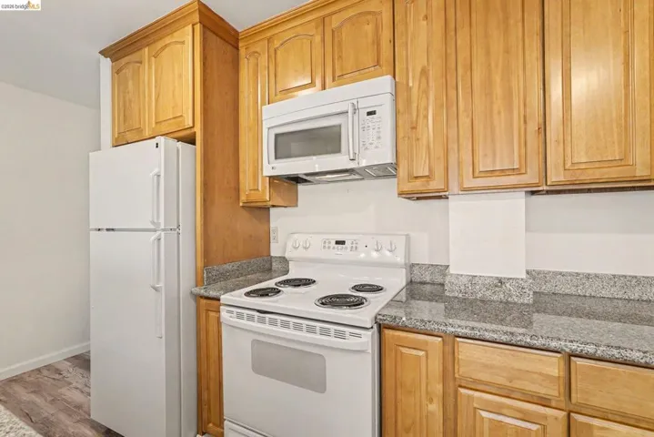 Kitchen featuring light wood cabinetry, stone-finish countertops, and white appliances including a refrigerator, range, and microwave