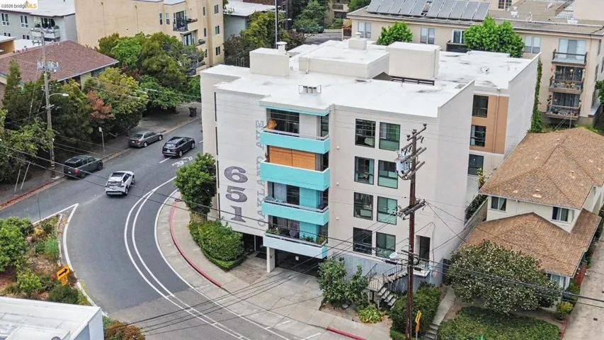Contemporary multi-story building featuring light-toned exterior siding, partial turquoise balcony railings, and multiple windows