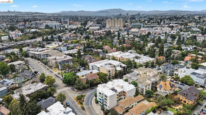 Urban landscape featuring diverse architectural styles, mature tree canopy, and distant mountains