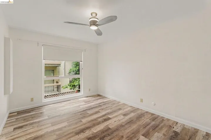 Bright room featuring wood-finish flooring, a large window, roller shade, and a ceiling fan with integrated lighting