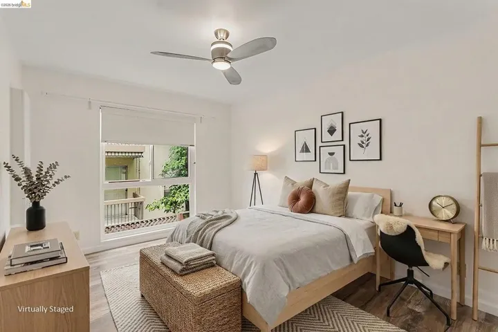 Well-lit bedroom featuring wood-finish flooring, a contemporary ceiling fan with integrated lighting, a large window, white walls, and a built-in recessed wall section